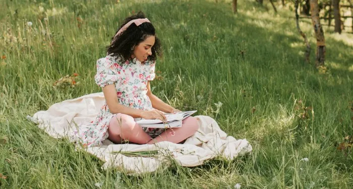 a Black woman reading on a blanket in a field